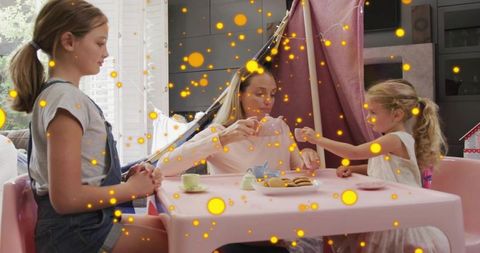 Mother pouring tea with daughters in pink blanket fort during cozy indoor playtime