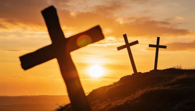Silhouetting three wooden crosses at sunset on grassy hill with golden lens flare