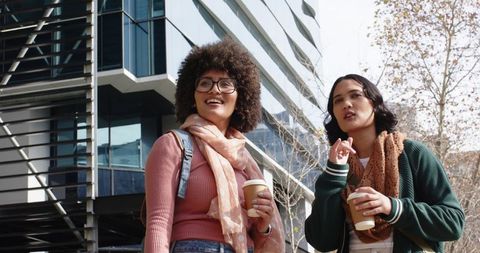 Diverse Women Laughing and Chatting Over Coffee in Plaza with Modern Glass Architecture