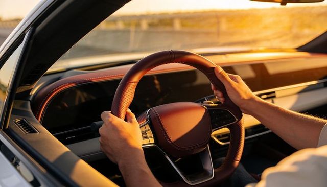 Hands gripping leather steering wheel during golden hour drive with modern dashboard glow