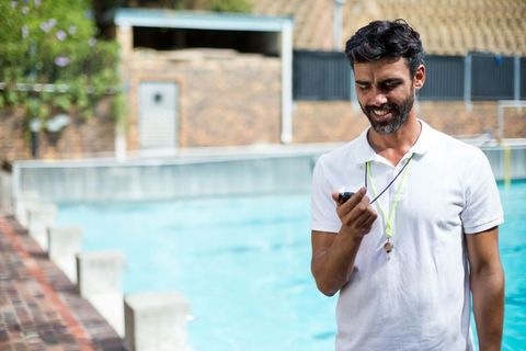 Male Swim Coach Using Phone Poolside During Training