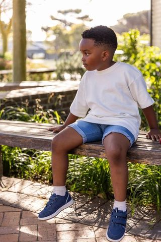 Contemplative african american boy sitting on wooden bench in park at golden hour