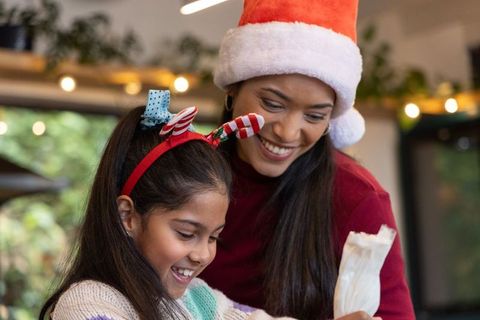 Mother and daughter decorating holiday cookies wearing santa hat and festive headband