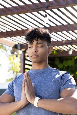 African american man meditating under pergola in sunlit backyard, promoting calm wellness