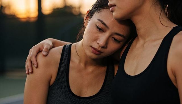 Two asian women embracing and resting after intense workout at sunset