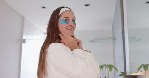 Woman enjoying self-care with blue eye patches in bathroom