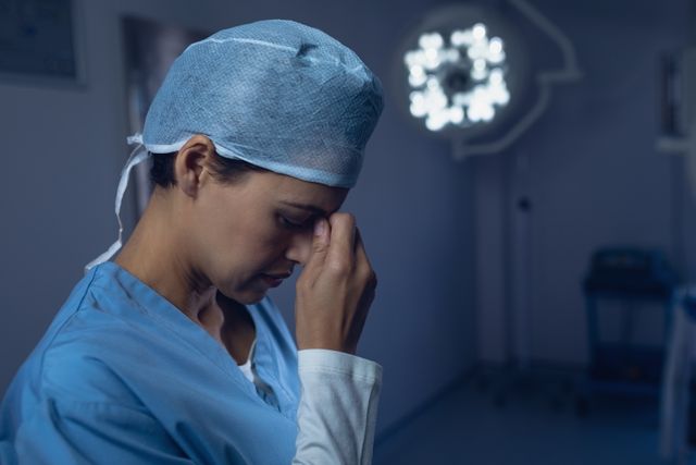 This image captures a stressed female surgeon taking a moment to rest in an operating room. Ideal for illustrating the challenging and stressful environment healthcare workers operate in, articles on medical professional burnout, and stress management in medical professions.