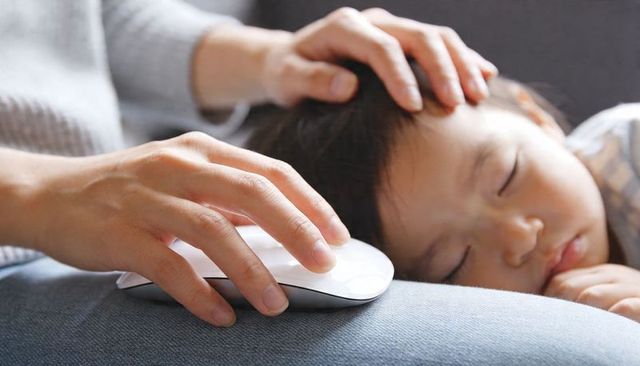 Parent soothing sleeping toddler while working with wireless mouse on lap