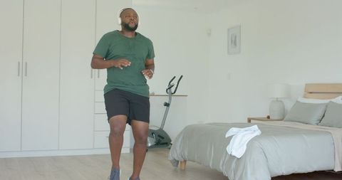 Man jogging in bright minimalist bedroom wearing headphones tracking home cardio progress