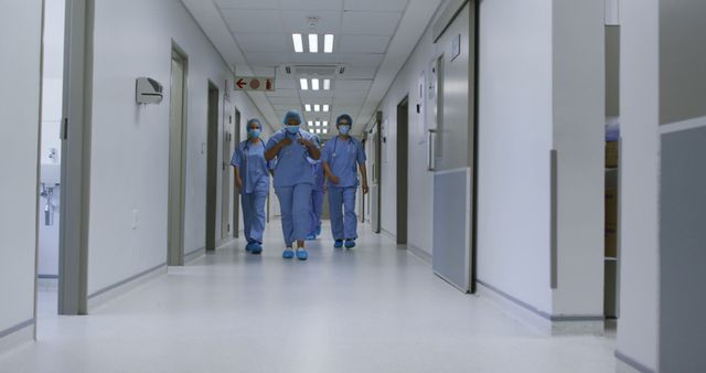 Healthcare workers walking down a hospital corridor in medical scrubs and masks. Useful for themes showing hospital environments, medical professionals, teamwork, healthcare facilities, and emergency response. Ideal for healthcare, medical, and hospital related content.