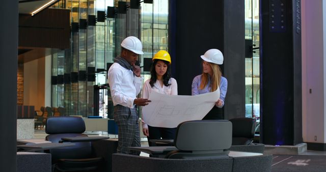 This captures a diverse team of male and female architects intently discussing blueprints in a modern office setting. Ideal for use in content promoting teamwork, diversity in the workplace, construction and architecture, and project planning. It can also effectively illustrate corporate collaboration or used in architectural or engineering firm websites.