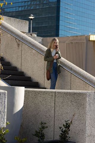 Young woman descending concrete stairs holding coffee and talking on phone at urban plaza