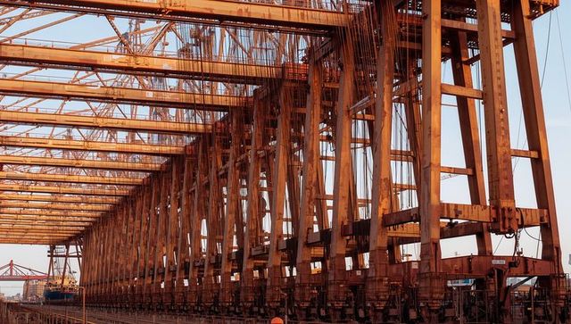 Rusted gantry crane spanning port dock at golden hour with worker in hi-vis helmet