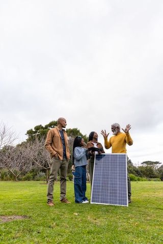 African american multigenerational family exploring solar panel technology on lawn