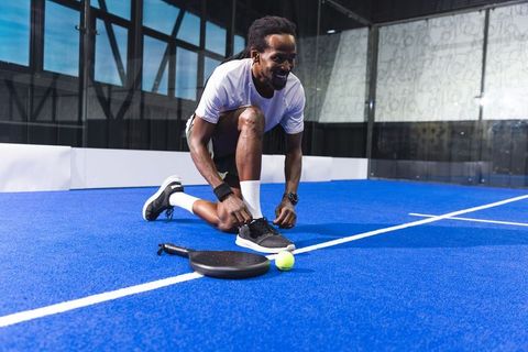 Athlete tying laces on padel court with racket and ball