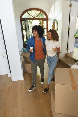 Young african american couple moving into new home holding coffee walking through foyer