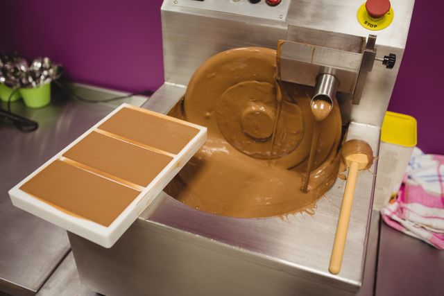 Mould filled with melted chocolate on blending machine in factory. Ideal for illustrating chocolate production, confectionery manufacturing, and industrial food processing. Useful for articles, advertisements, and educational materials related to chocolate making and factory operations.