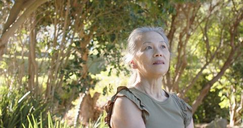 Senior chinese woman gazing upward in sunlit garden, peaceful nature portrait