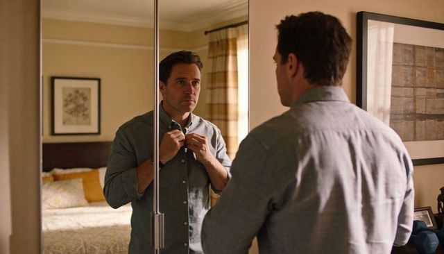 Middle-aged man fastening top button while looking in mirrored wardrobe morning routine