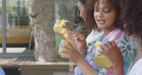 African american women chatting and holding lemonade on sunny outdoor terrace in summer