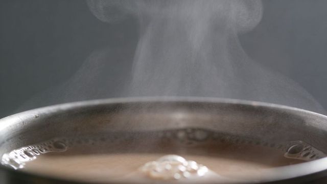 Steaming stainless pot rim with rising vapor and frothy brown liquid macro kitchen detail