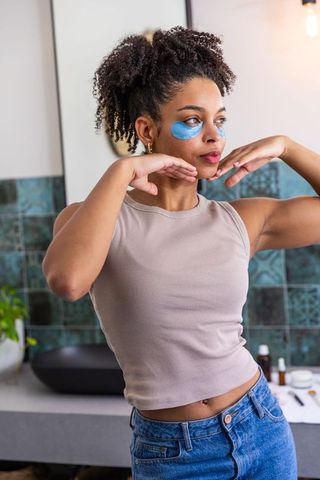 African american woman at vanity wearing blue under-eye patches practicing self-care