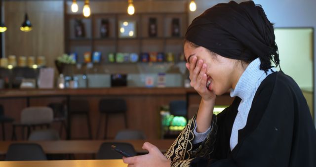 Young Woman Wearing Traditional Outfit Laughing While Reading Message in Cafe - Download Free Stock Images Pikwizard.com