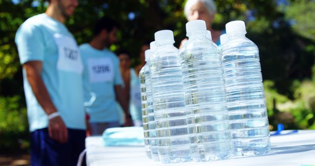 Bottled water is in focus in the foreground, with diverse volunteers or event participants blurred in the background, with copy space. Providing hydration at community events or sports activities is essential, and this setup suggests preparation for such an occasion.