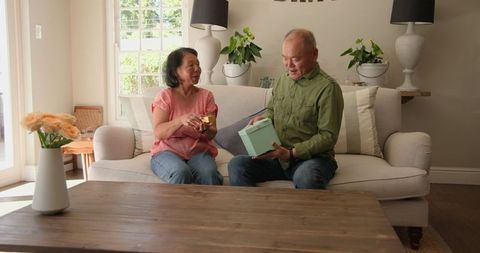 Senior Couple Smiling While Unwrapping Gift Together on Couch