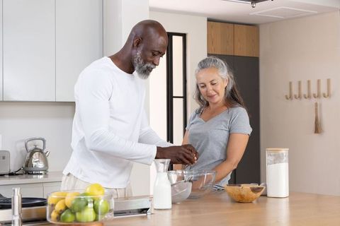 Mature diverse couple cooking together in modern kitchen, man cracking egg into bowl