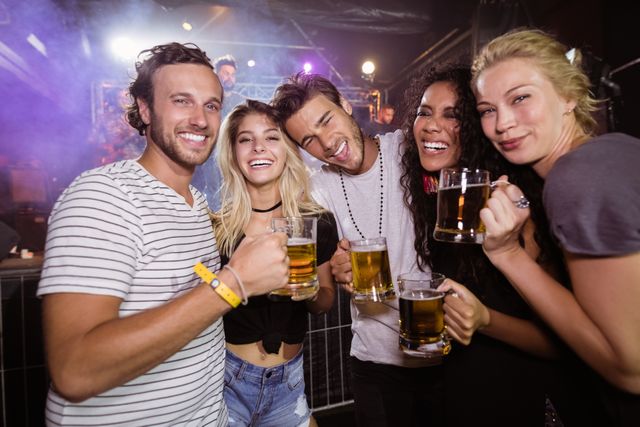 Portrait of smiling friends holding beer mugs while standing together at nightclub