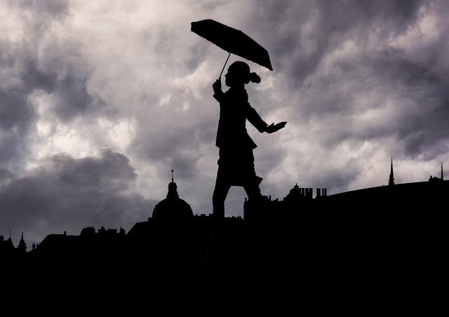 Silhouette of woman holding umbrella walking against stormy clouds