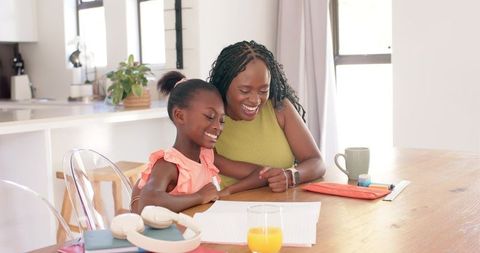 African american mother and daughter studying together at sunlit kitchen table