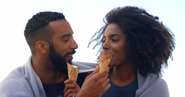 Romantic diverse couple with blankets on backs eating ice creams, copy space. Summer, vacation, romance, love, relationship, free time and lifestyle, unaltered.