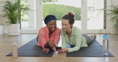 Diverse friends relaxing together on yoga mats while using smartphone