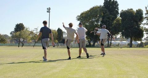 Diverse men warming up on sunlit community sports field with yellow training cone