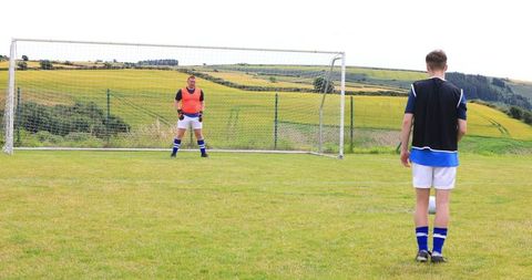 Teammates practicing soccer with goalkeeper on rural field