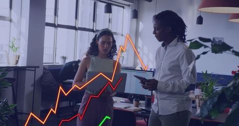 Collaborative team analyzing fluctuating line charts on laptop and smartphone in office