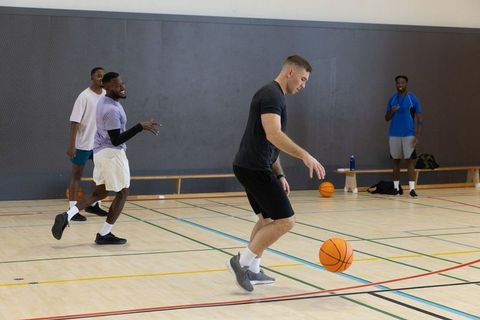 Four men dribbling basketballs on indoor gym court during casual recreational pickup game