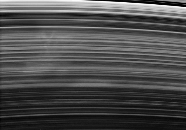 Saturn's B ring is shown with a ghostly spoke drifting past, showcasing faint longitudinal brightness variations captured by the Cassini spacecraft. This intriguing phenomenon is a subject of scientific study, and images like this can be utilized in educational materials, space exploration articles, astronomy presentations, and astrophotography collections.