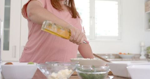 Plus Size Woman Preparing Salad with Olive Oil in Modern Kitchen