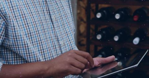 Middle-aged man using tablet while browsing wine bottles in boutique wine shop