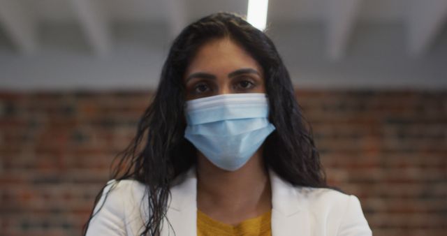This image shows a confident woman wearing a face mask in an office setting. Ideal for business-related posts, articles on professional women, workplace safety, COVID-19 guidelines, and health precautions in corporate environments.
