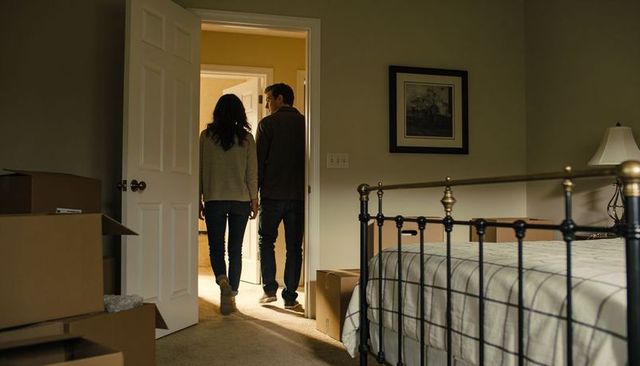 Couple wearing sweaters and jeans walking through bedroom doorway during moving with boxes