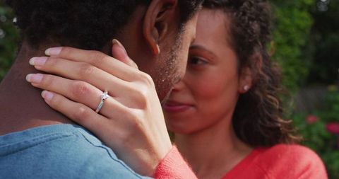 Close-up of woman's hand with engagement ring embracing partner