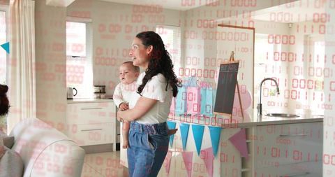 Smiling mother holding baby during gender reveal celebration in bright modern kitchen