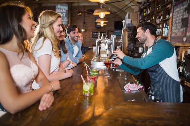 Bartender engaging with a group of friends at a bar, making drinks and creating a lively atmosphere. Ideal for use in advertisements for bars, nightlife promotions, hospitality industry, and social event marketing.