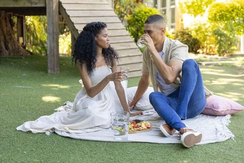 Couple enjoying backyard picnic on blanket, sharing fruit and water, relaxing outdoors