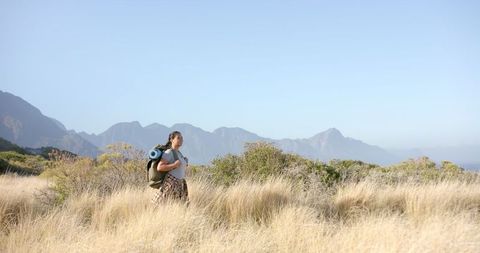 Woman Hiking with Backpack and Yoga Mat in Scenic Grassland