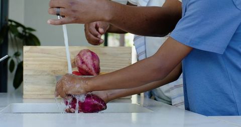 African american father and son washing purple yams at kitchen sink, family cooking moment